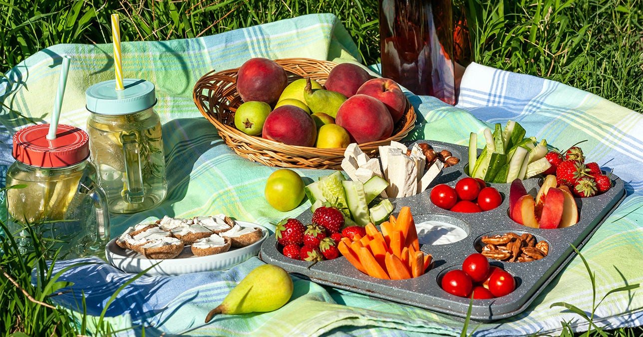 Picnic spread with homemade snacks, fruit and drinks on a blanket outdoors.