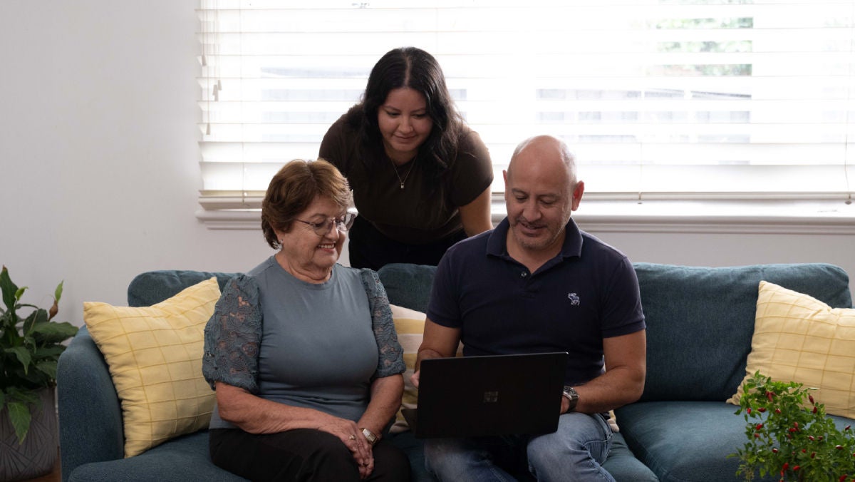 Three individuals sitting on a couch in a bright living room, looking at a laptop together reading about SMSF loans