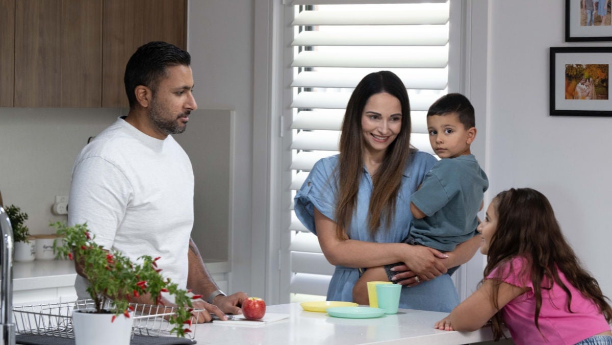 Family standing around a kitchen bench with adults and children at home.